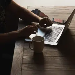 Osoba pracuje na laptopie, sprawdzając wymagania Unreal Engine 5. Obok kubek i telefony.