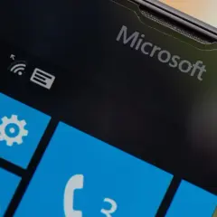 Ekran telefonu z logo Microsoft i kafelkami interfejsu Windows Mobile. Widoczne ikony wiadomości, ustawień, poczty i telefonu.