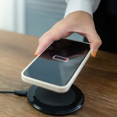 Dłoń kładzie telefon z niskim stanem baterii na ładowarce bezprzewodowej.