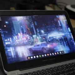 Laptop z systemem Vanilla OS, na ekranie futurystyczne miasto nocą, deszcz i samochód DeLorean.