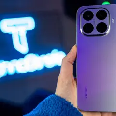 Fioletowy Xiaomi 15T Pro z potrójnym aparatem Leica w dłoni, na tle niebieskiego logo.