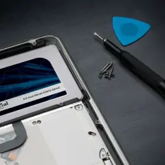 Wymiana dysku na **Crucial MX500 4TB** w laptopie. Obok śrubokręt, śrubki i niebieski pick.