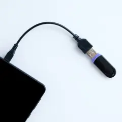 Czarny pendrive podłączony do telefonu przez kabel. Tak, można podłączyć pendrive do telefonu, by przenieść dane.