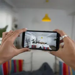 Podgląd z kamery w telefonie pokazuje jasne, nowoczesne wnętrze z żółtą lampą i stołem.