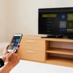 Osoba używa iPhone'a do sterowania telewizorem, pokazując, jak udostępnić ekran z iPhone na TV.