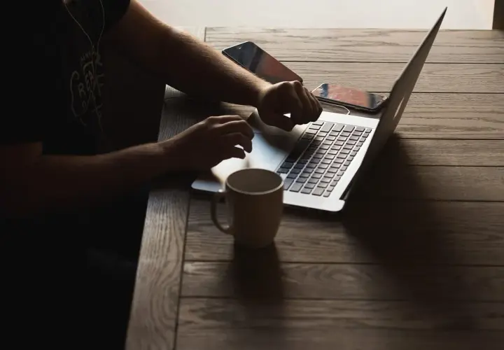 Osoba pracuje na laptopie, sprawdzając wymagania Unreal Engine 5. Obok kubek i telefony.