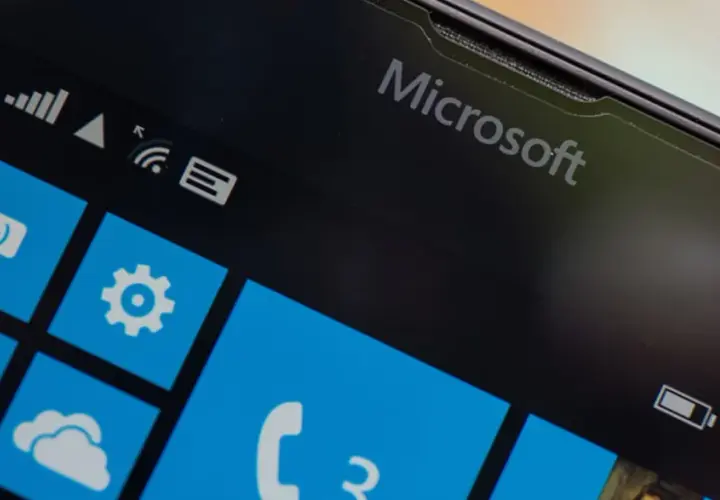 Ekran telefonu z logo Microsoft i kafelkami interfejsu Windows Mobile. Widoczne ikony wiadomości, ustawień, poczty i telefonu.