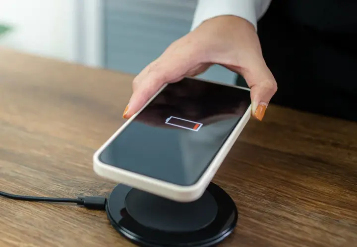 Dłoń kładzie telefon z niskim stanem baterii na ładowarce bezprzewodowej.