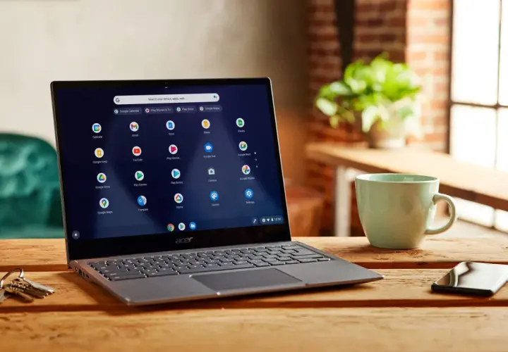 Laptop z systemem Chrome OS instalacja. Na ekranie widoczne ikony aplikacji Google. Obok kubek i klucze.
