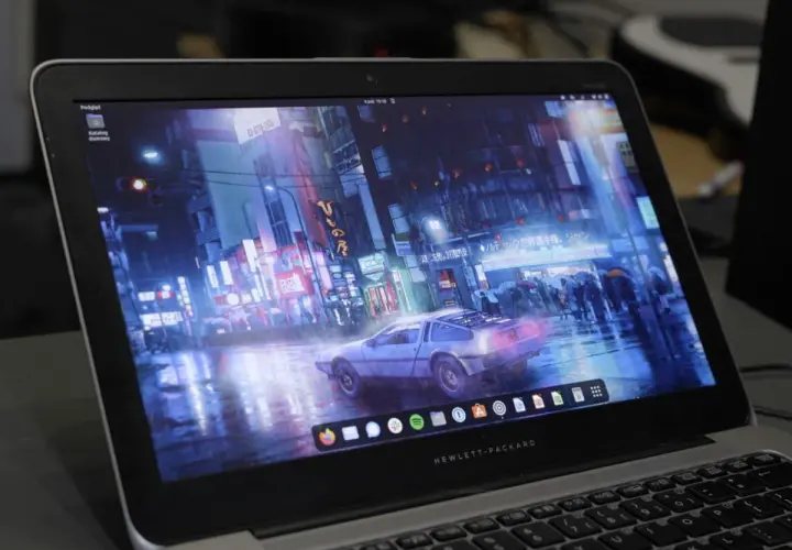 Laptop z systemem Vanilla OS, na ekranie futurystyczne miasto nocą, deszcz i samochód DeLorean.