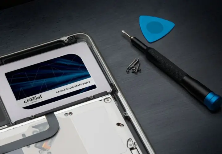 Wymiana dysku na **Crucial MX500 4TB** w laptopie. Obok śrubokręt, śrubki i niebieski pick.