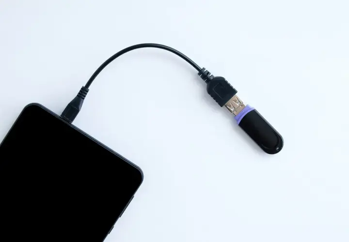 Czarny pendrive podłączony do telefonu przez kabel. Tak, można podłączyć pendrive do telefonu, by przenieść dane.