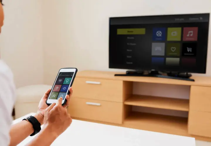 Osoba używa iPhone'a do sterowania telewizorem, pokazując, jak udostępnić ekran z iPhone na TV.