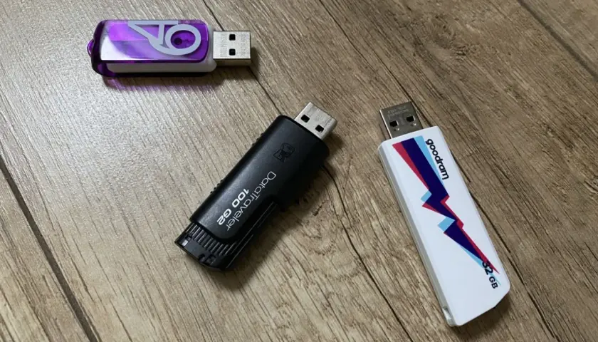 Trzy pendrive'y na drewnianym tle. Jeden fioletowy z logo, czarny DataTraveler 100 GB i biały Goodram 32 GB. Szybki pendrive 64 GB to marzenie!