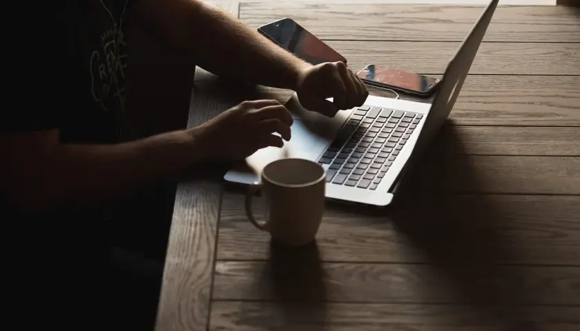 Osoba pracuje na laptopie, sprawdzając wymagania Unreal Engine 5. Obok kubek i telefony.