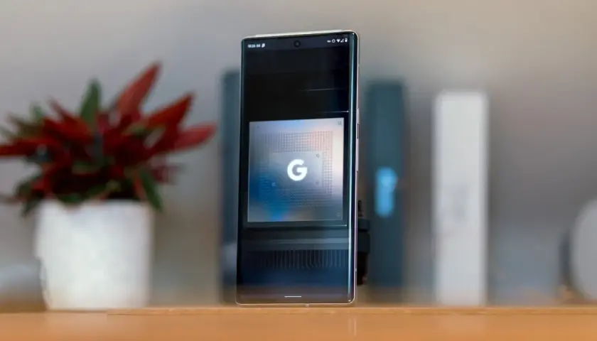 Smartfon z ekranem prezentującym układ Google Tensor G5. Obok stoi doniczka z czerwoną rośliną.