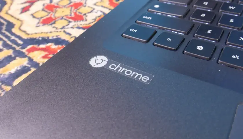 Naklejka z logo Chrome na ciemnym laptopie, obok klawiatury. System Chrome działa płynnie.
