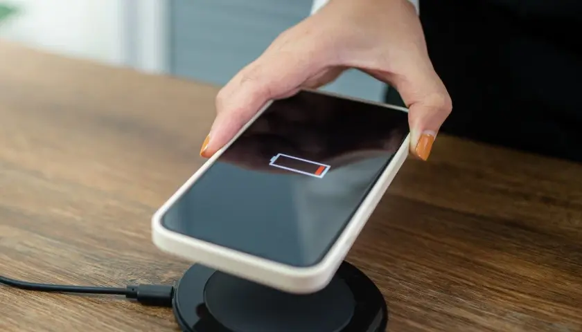 Dłoń kładzie telefon z niskim stanem baterii na ładowarce bezprzewodowej.