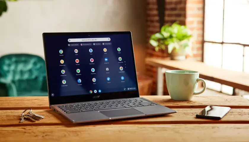 Laptop z systemem Chrome OS instalacja. Na ekranie widoczne ikony aplikacji Google. Obok kubek i klucze.