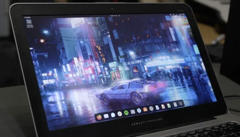 Laptop z systemem Vanilla OS, na ekranie futurystyczne miasto nocą, deszcz i samochód DeLorean.