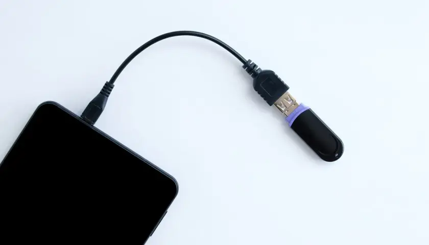 Czarny pendrive podłączony do telefonu przez kabel. Tak, można podłączyć pendrive do telefonu, by przenieść dane.