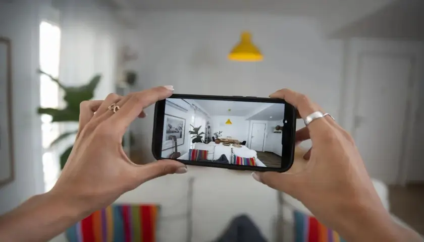 Podgląd z kamery w telefonie pokazuje jasne, nowoczesne wnętrze z żółtą lampą i stołem.