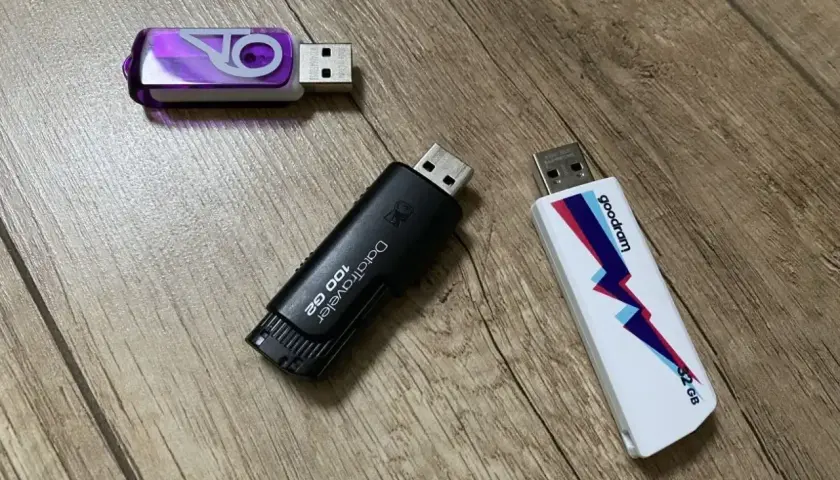 Trzy pendrive'y: fioletowy z logo, czarny DataTraveler 100 GB i biały Goodram 32 GB.