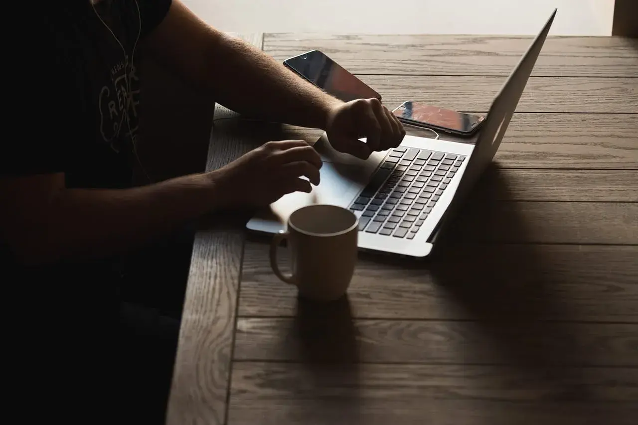 Osoba pracuje na laptopie, sprawdzając wymagania Unreal Engine 5. Obok kubek i telefony.