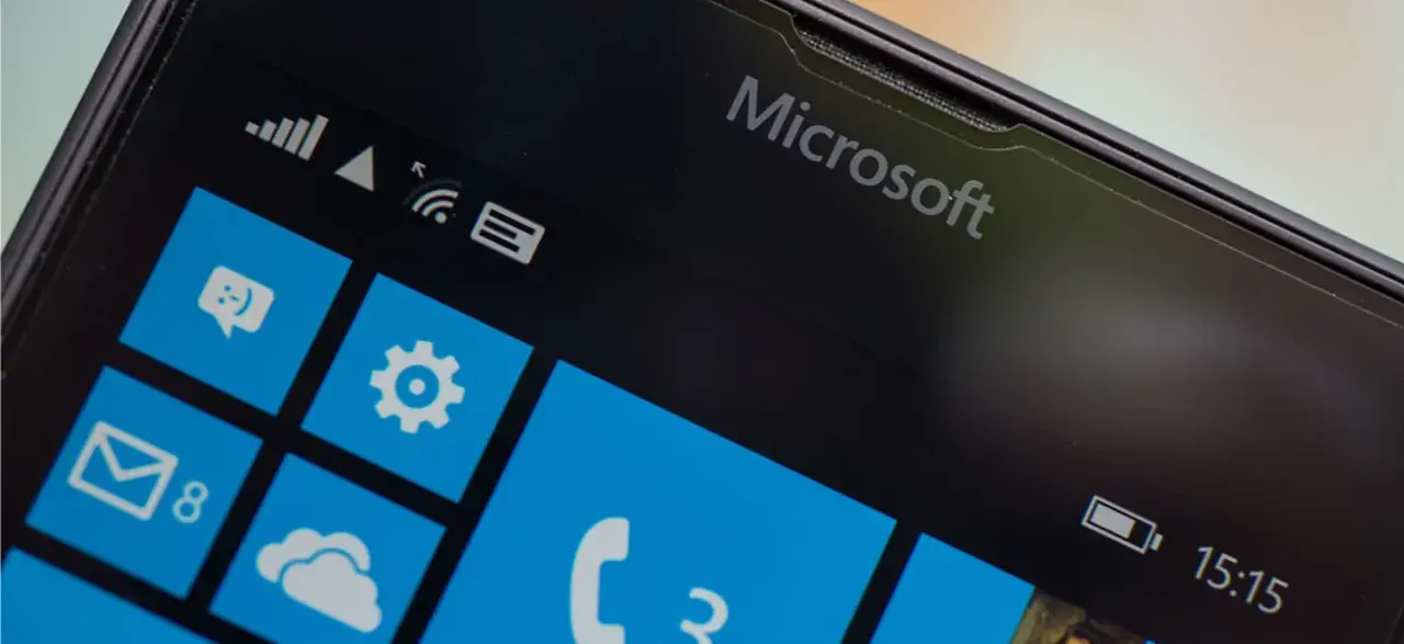 Ekran telefonu z logo Microsoft i kafelkami interfejsu Windows Mobile. Widoczne ikony wiadomości, ustawień, poczty i telefonu.