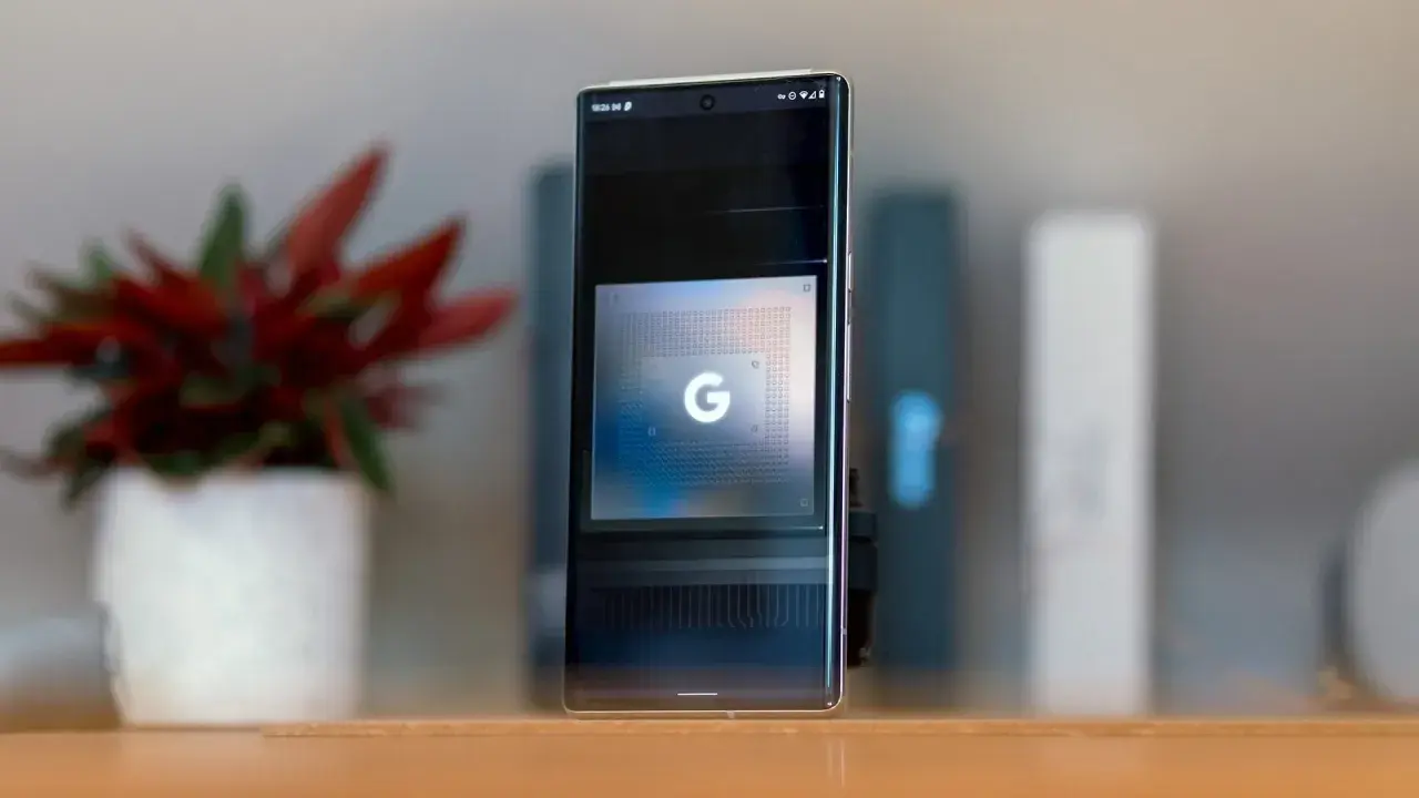 Smartfon z ekranem prezentującym układ Google Tensor G5. Obok stoi doniczka z czerwoną rośliną.