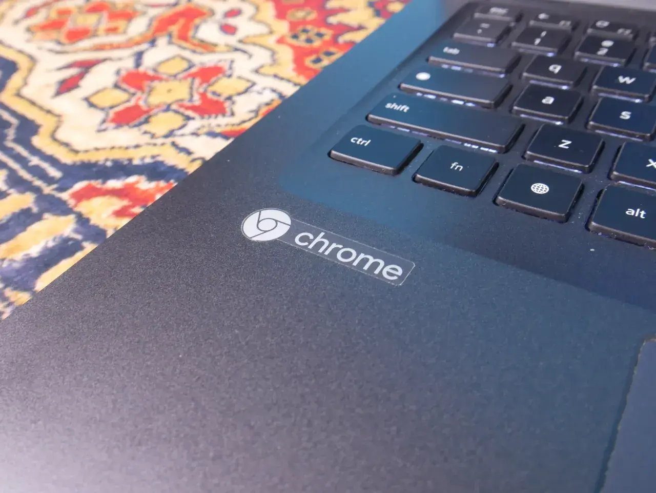 Naklejka z logo Chrome na ciemnym laptopie, obok klawiatury. System Chrome działa płynnie.
