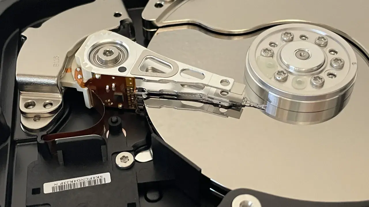 Wnętrze dysku twardego, przygotowanego do testu ssd. Widoczne talerze, głowice i mechanizm pozycjonujący.