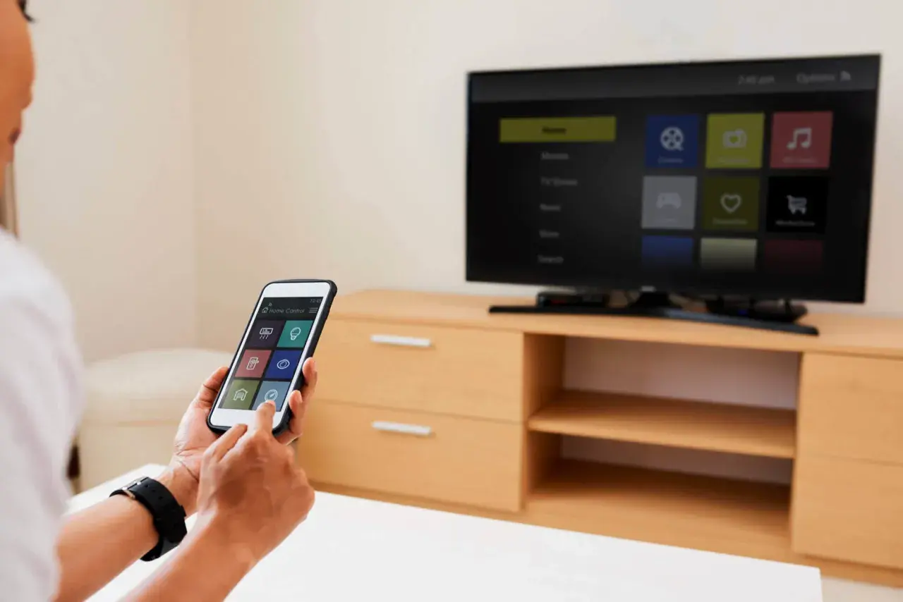 Osoba używa iPhone'a do sterowania telewizorem, pokazując, jak udostępnić ekran z iPhone na TV.