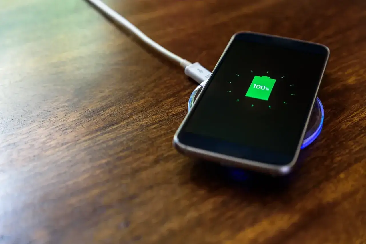 Smartfon na ładowarce indukcyjnej z 100% baterii. Dowiedz się, jak dbać o baterie w telefonie, by służyły dłużej.