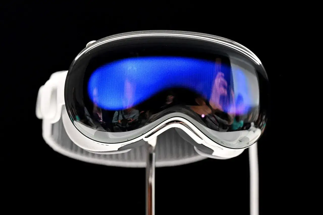 Nowe gogle Apple Vision Pro 2 z niebieskim ekranem, odbijające sylwetki ludzi.
