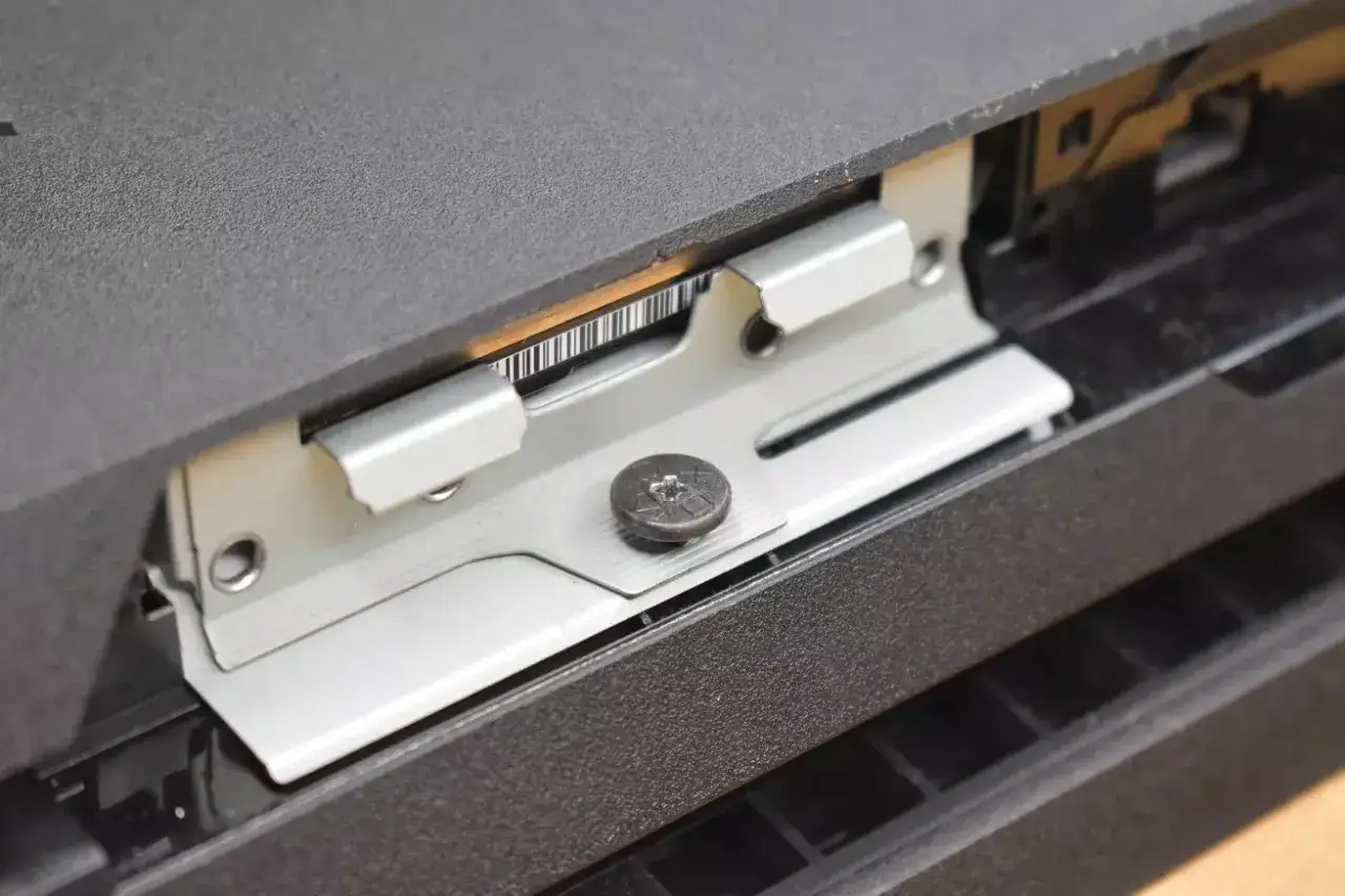 Metalowa ramka mocująca dysk SSD w konsoli PS4, widoczny wkręt.