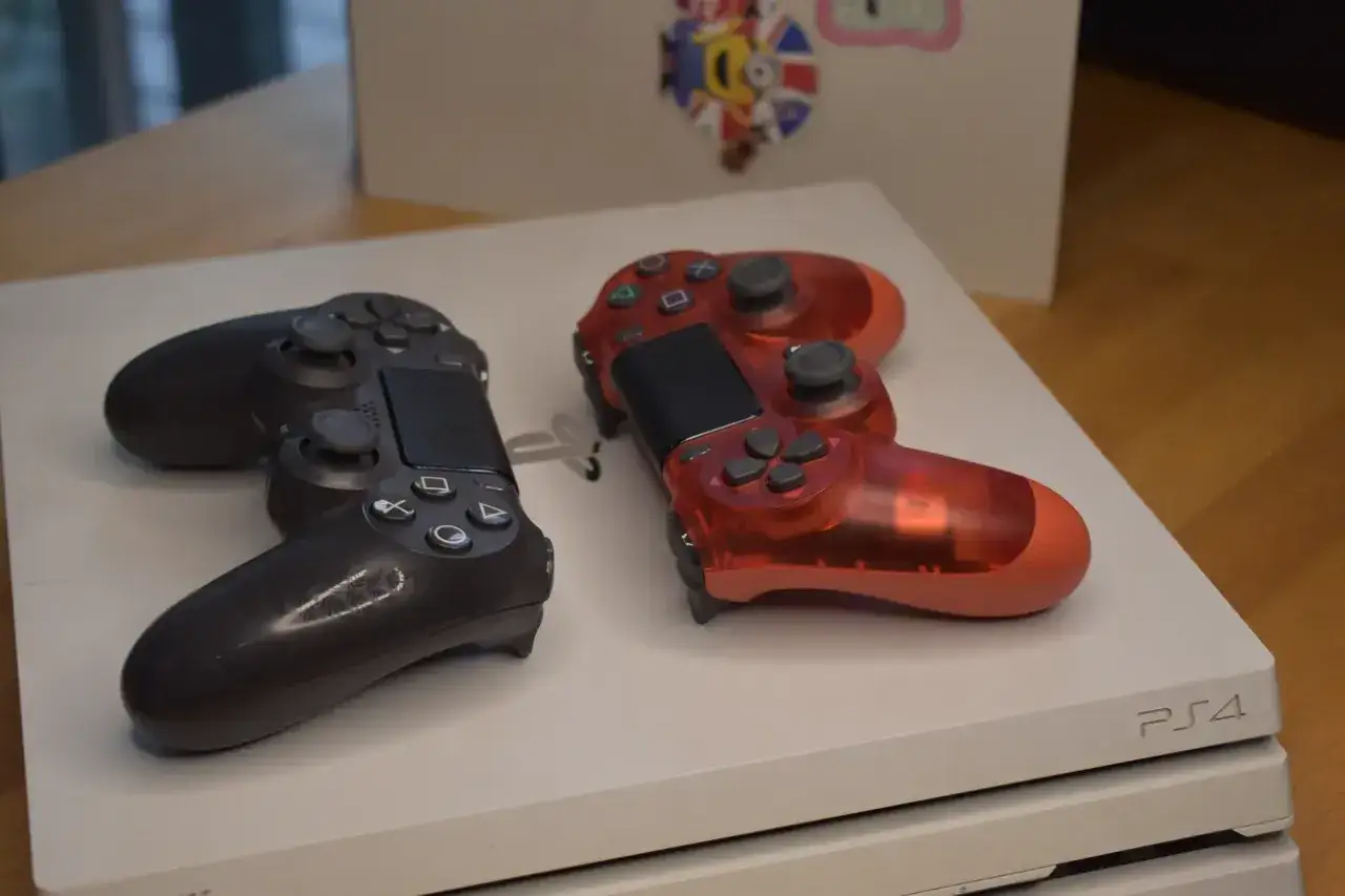 Dwa kontrolery, czarny i czerwony, leżą na białej konsoli PS4. Gotowi na premierę PS4!
